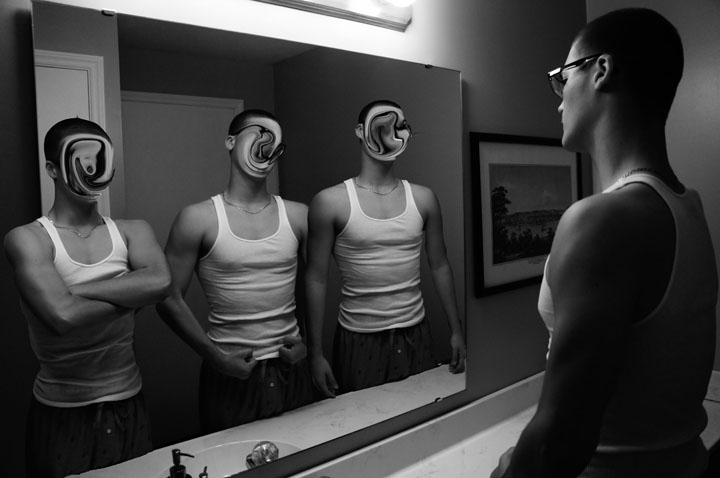 A man in an undershirt looks in the mirror, where three versions of himself with blurred faces and different postures look back.