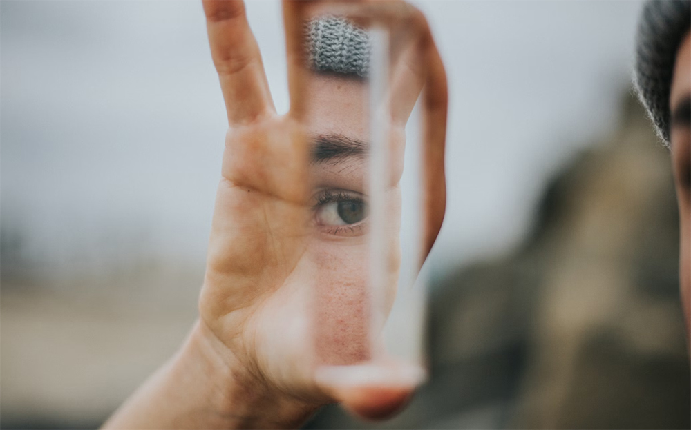 An image of a hand holding a small mirror that is reflecting one of the holder's eyes, eyebrows, and cheeks.