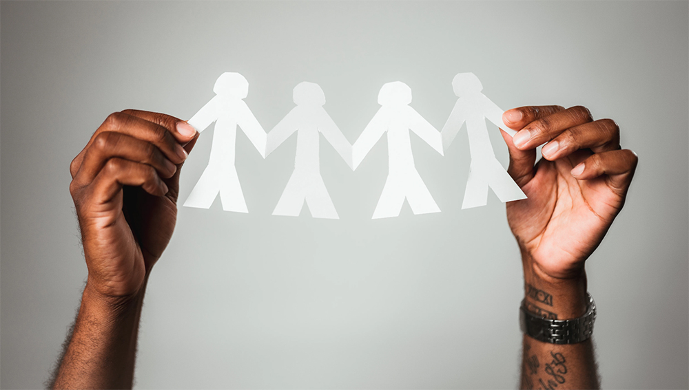 An image of two hands holding a white paper cutout of four stick figure people holding hands.