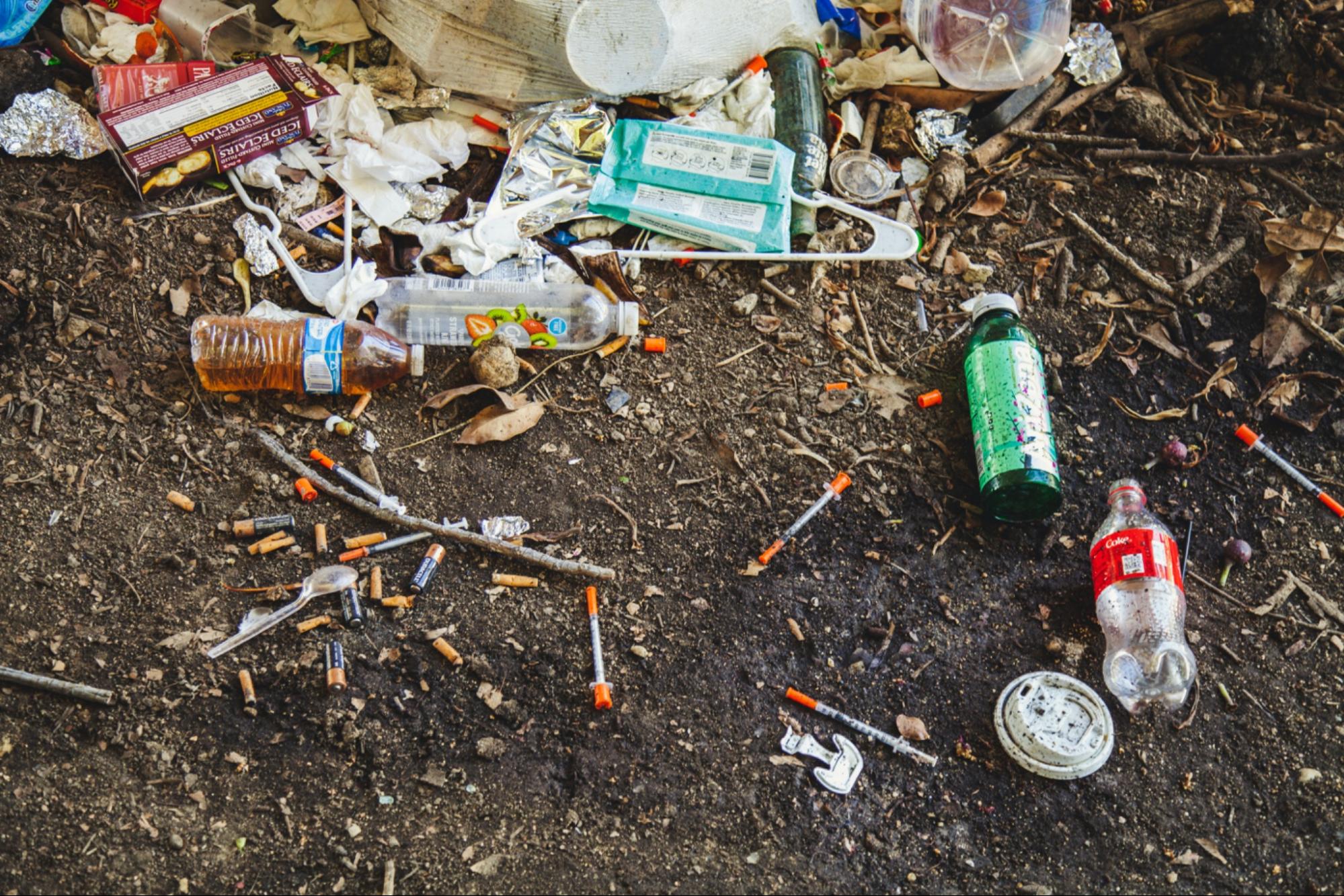 garbage on the ground including empty beverage bottles, syringes, and food wrappers.