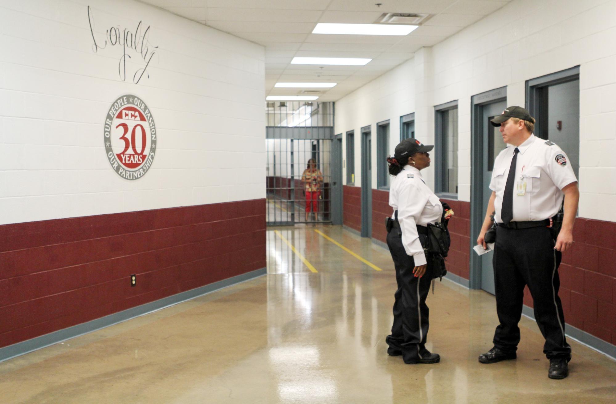 One correctional officer speaks t another the the hallway of a facility.