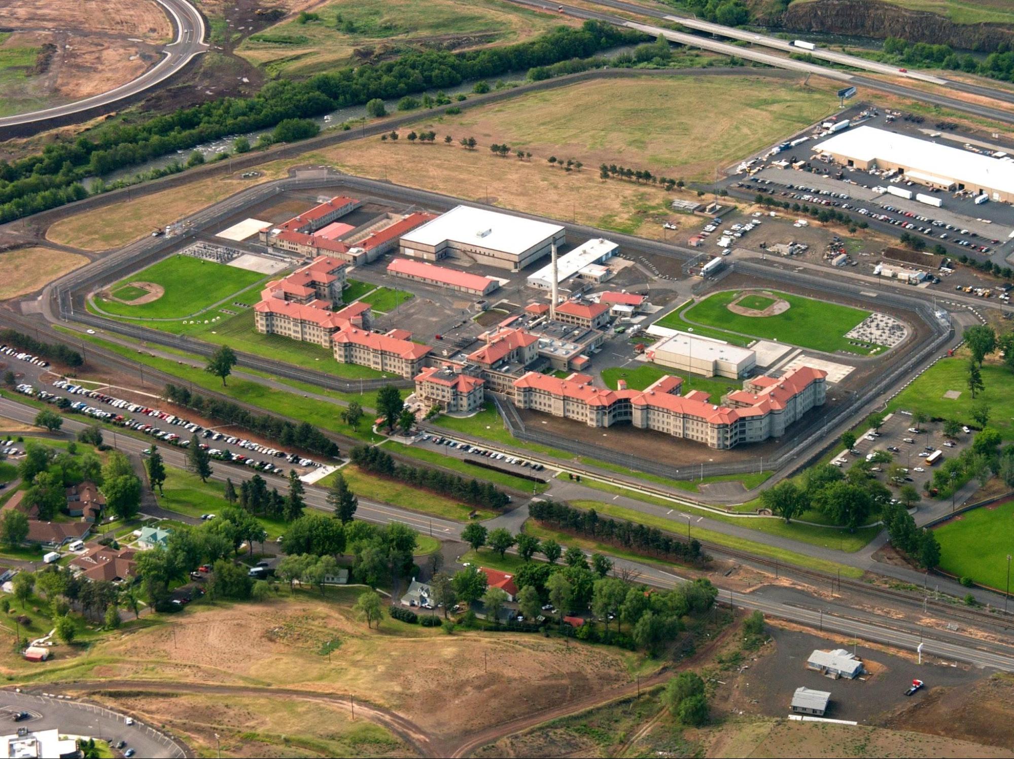 Overhead view of The Eastern Oregon Correctional Institution in Pendleton, Oregon. Many buildings and 2 sports fields surrounded by heavy fences in the middle of what looks to be rural land.