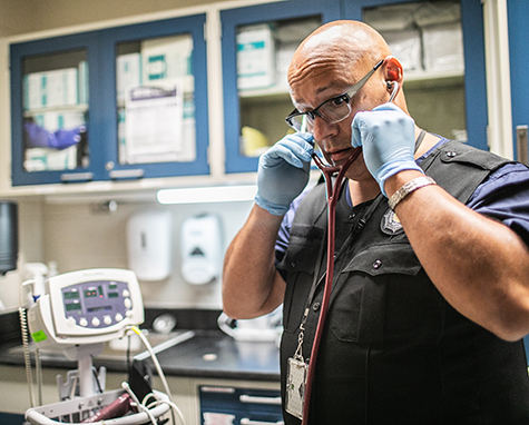 A medical worker in a prison holds a stethoscope to his ears.