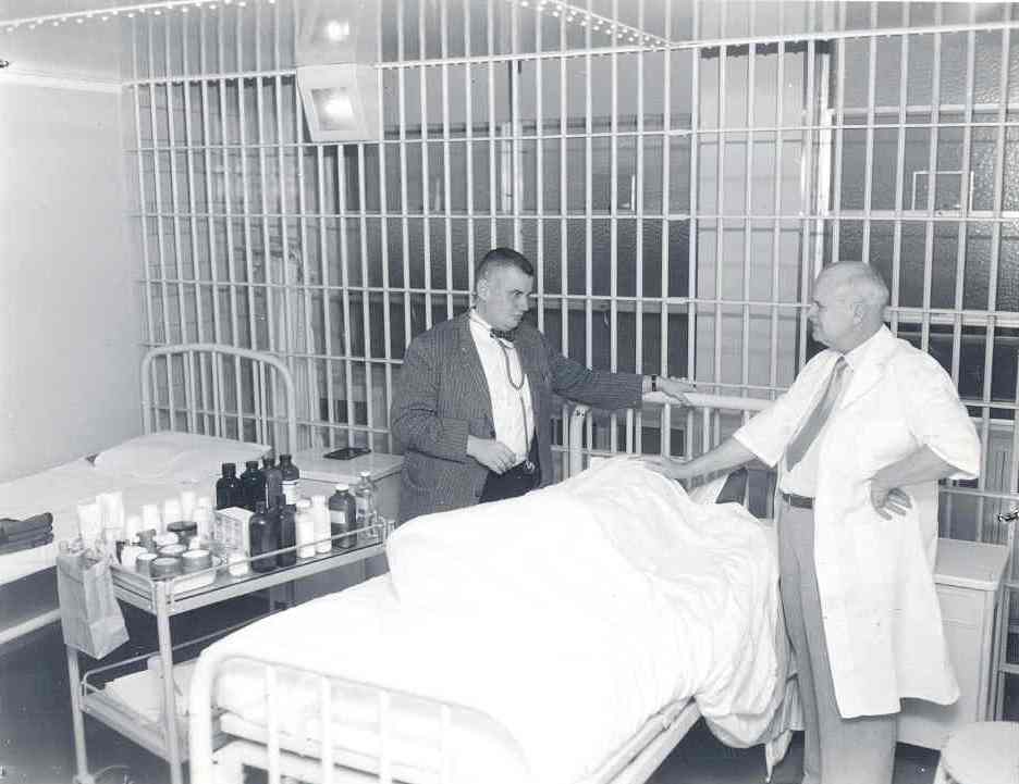 Historical photo of two doctors standing over an unseen person in a bed.