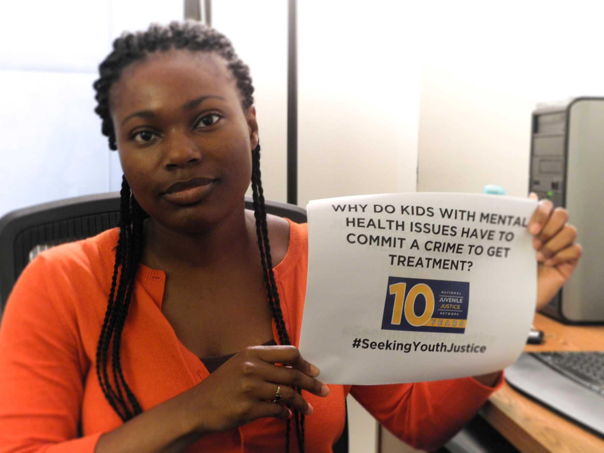 A woman holding a sign that reads "Why do kids with mental health issues have to commit a crime to get treatment?"