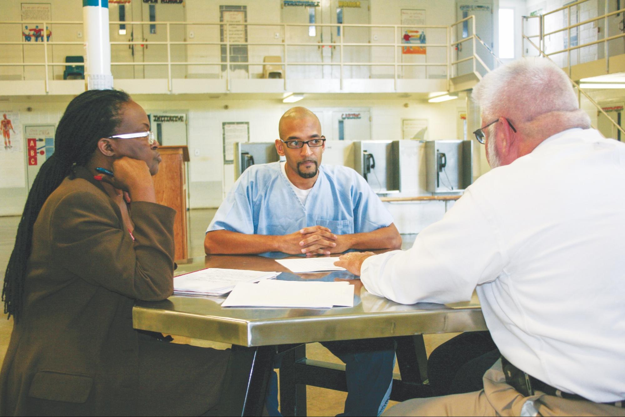 a person in custody conferring with facility staff at a table in the middle of a facility