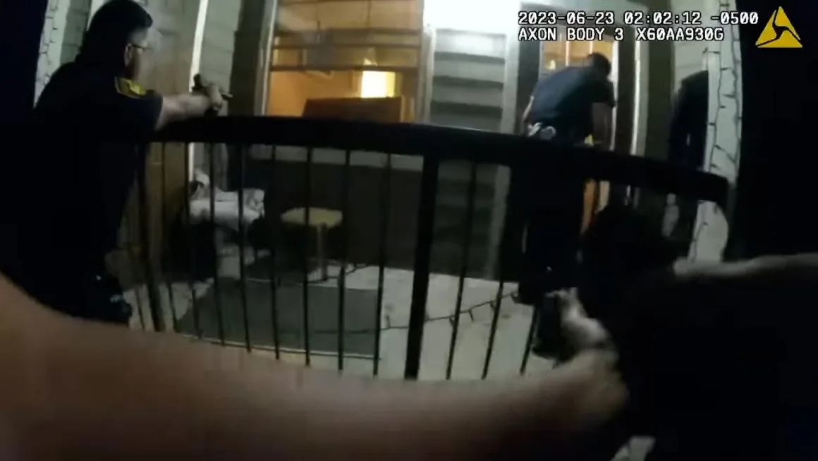 First-person camera view of officers on a porch. The person wearing the camera's arms are outstretched and pointing a gun. A second officer is also pointing a gun. The third officer is at the door.