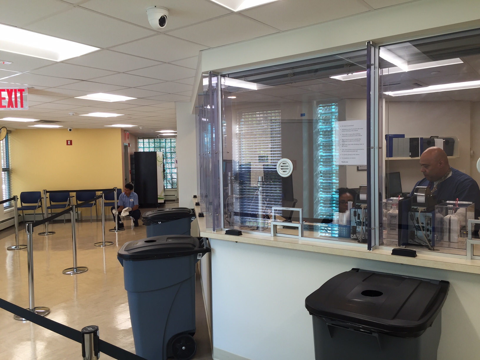 a walk-up window in a community clinic for providing medications for substance use treatment. A worker sits behind a window and patients come and walk up to receive their medication.