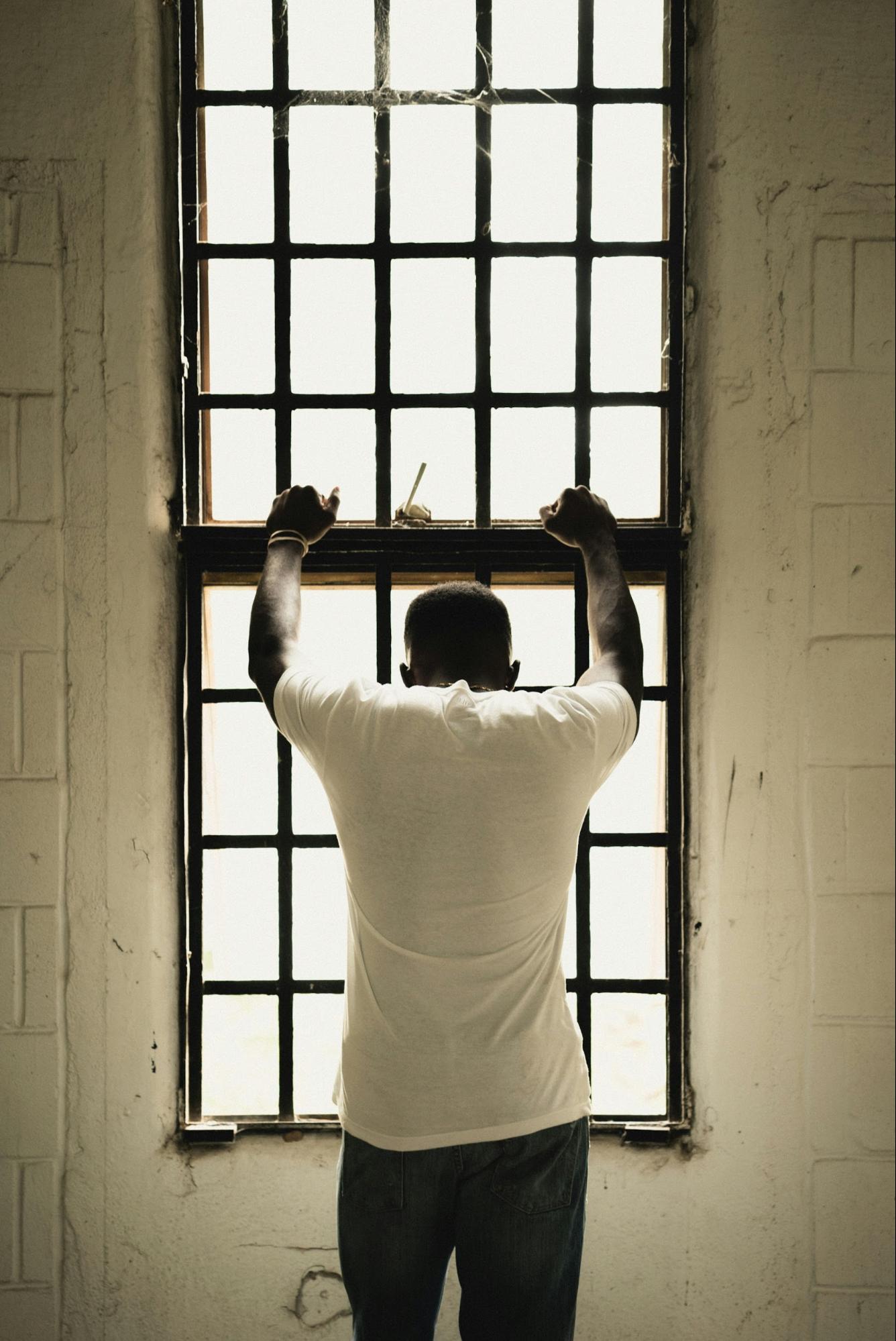 A man in an anguished pose and with his back to camera looking out a window