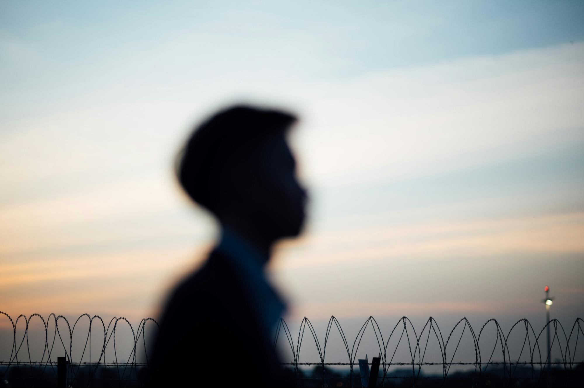 the outline of a person walking outside of prison fencing.