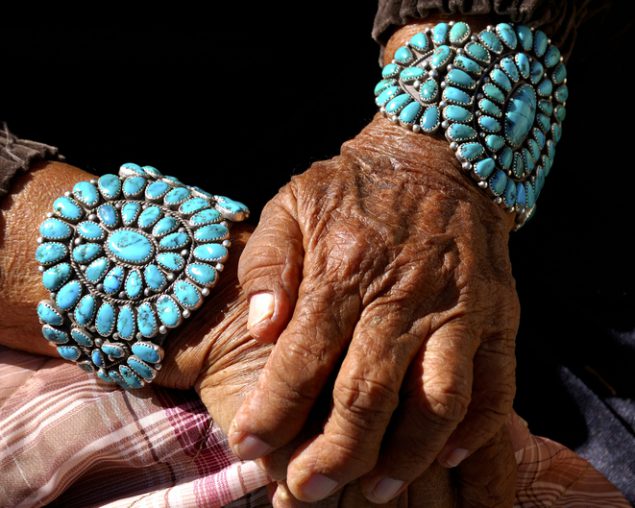 hands of an older person with brown skin, wrists adorned with traditional jewelry.