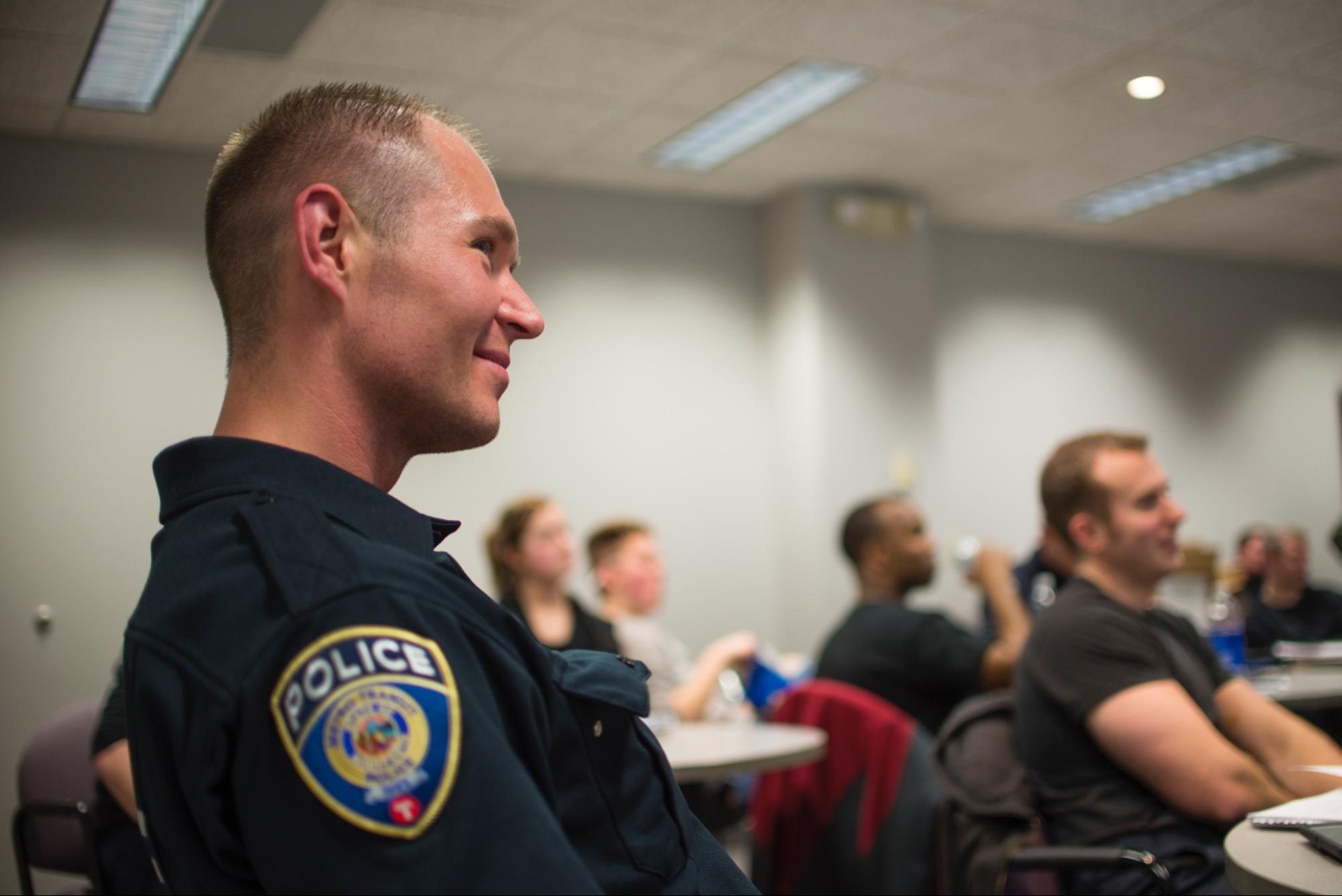 Police officer in uniform in a classroom smiling while listening