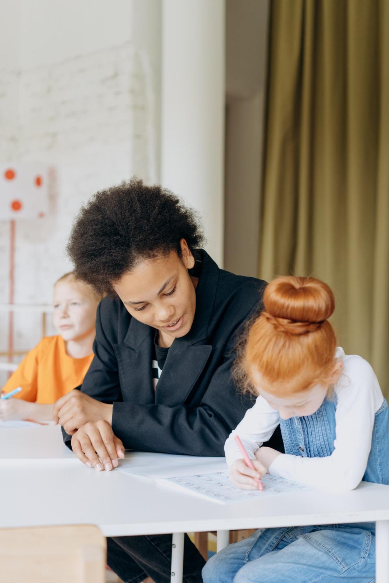 A child writes on paper while an adult helps her.