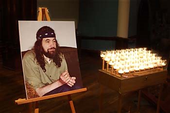 Photo showing a painted portrait on an easel, next to a rack of votive candles