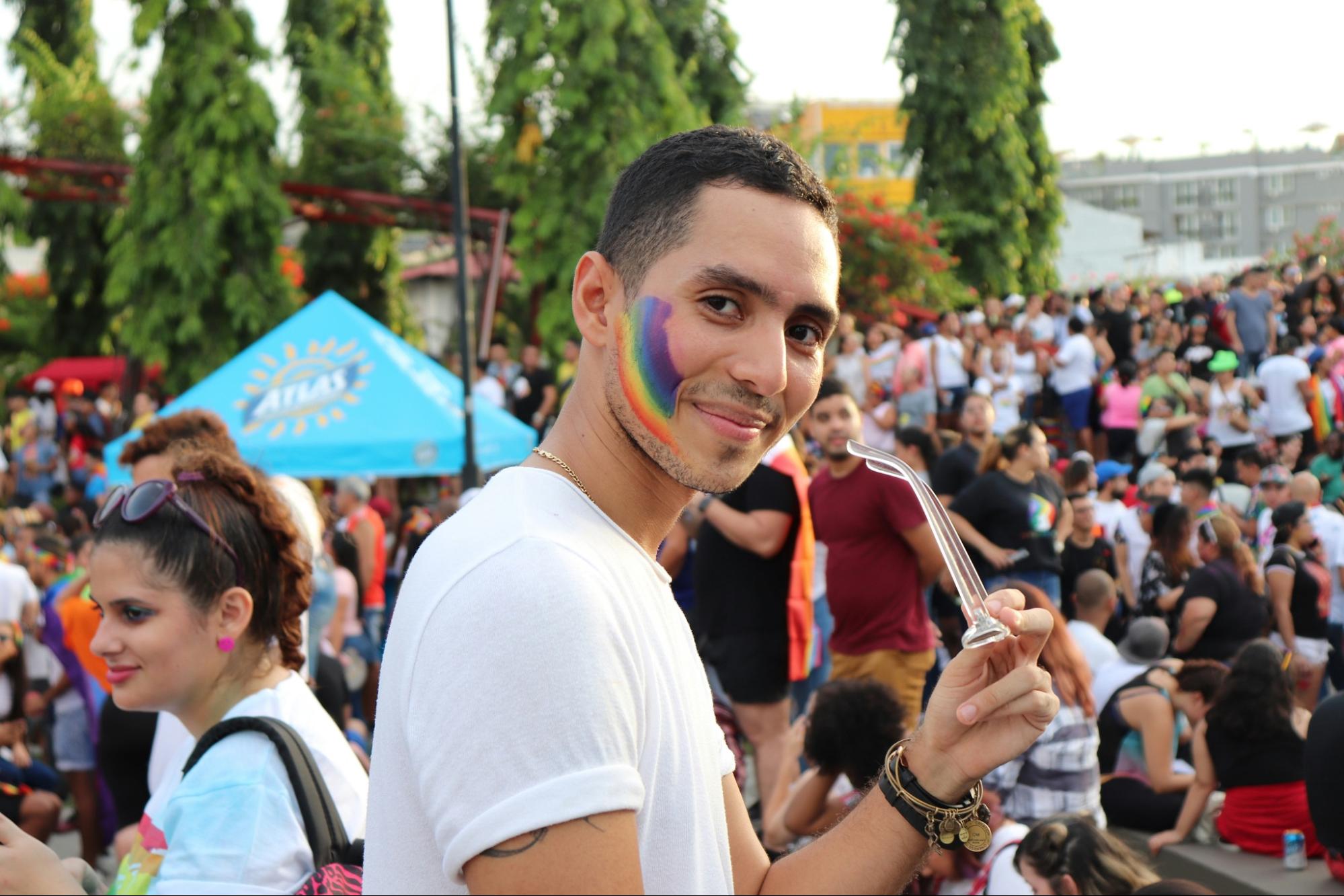 a person with a rainbow face decoration smiling in a crowd at a Pride event.