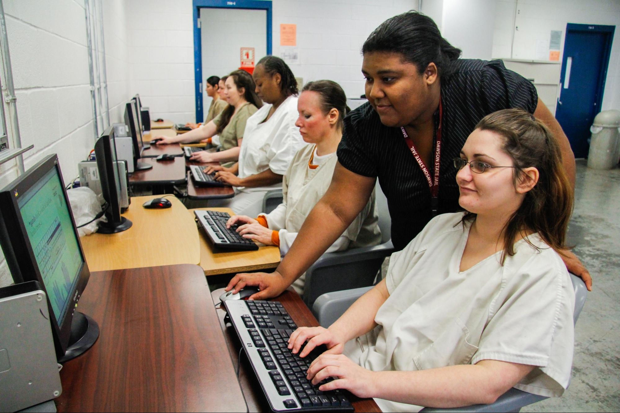 Photo of people wearing prison uniforms using computers.