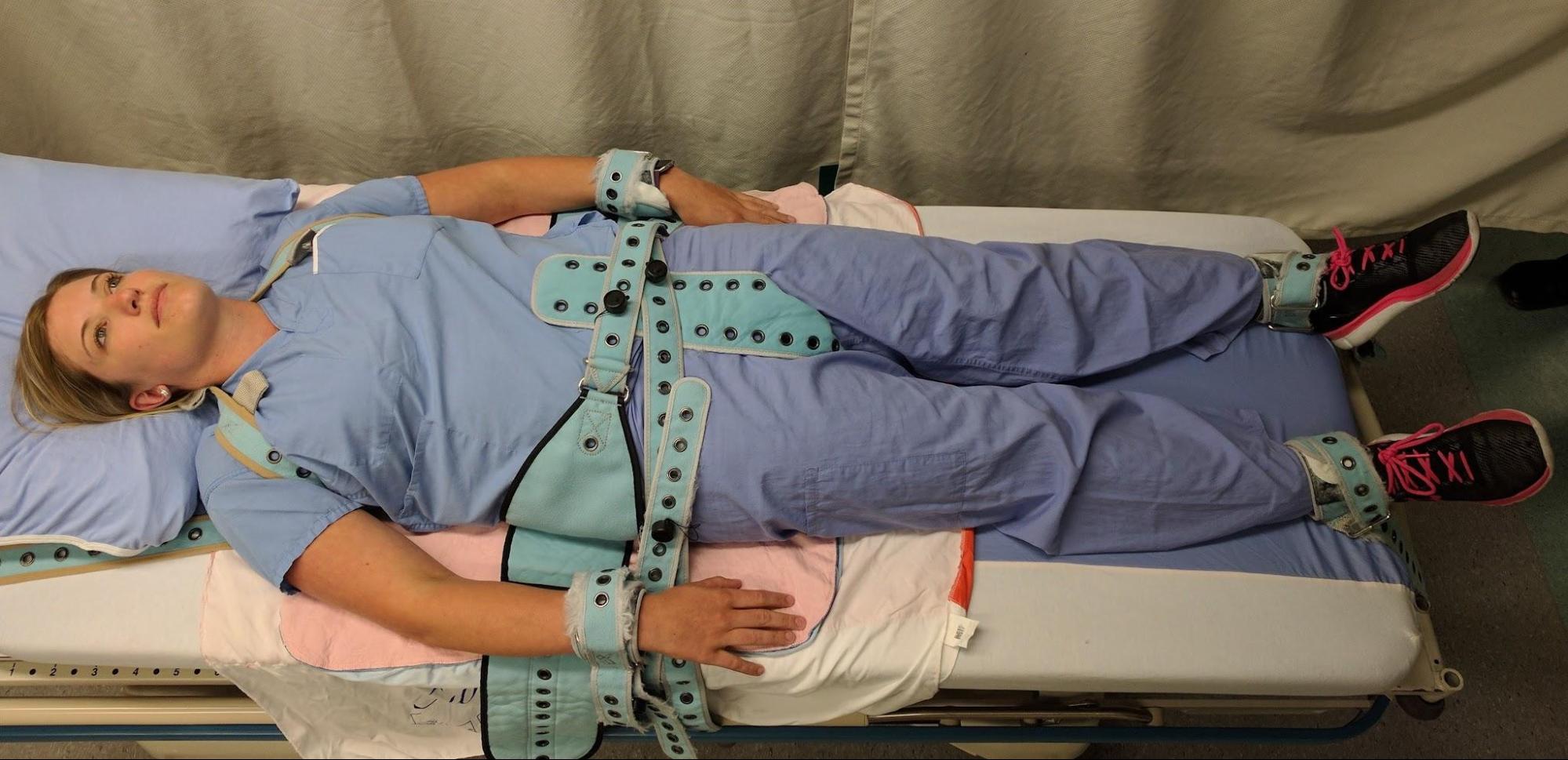 A person in Pinel restraints with their shoulders, waist, wrists, and ankles strapped to the bed.