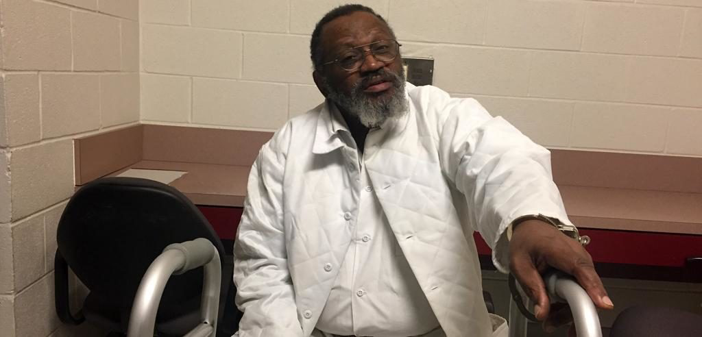 Vernon Madison sits with a walker while wearing a handcuff