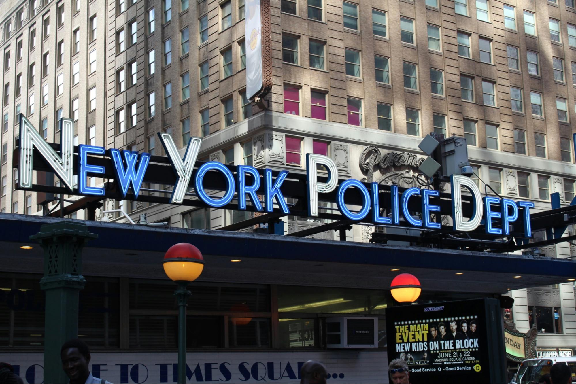 Photo of a neon sign above a subway station that says "New York Police Dept".