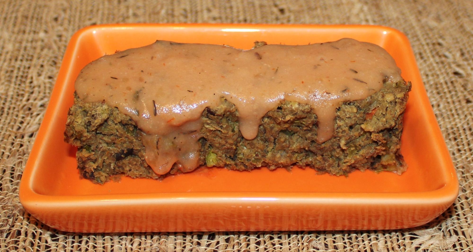 A brown square of prison loaf with gravy on top, on an orange plate.