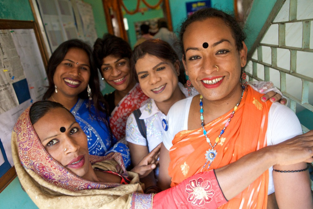 A group of people in saris, bindis, and head scarves smiles for a photo.