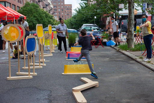 Photo of a kid playing on a city street that has been blocked off to traffic by colorful barriers.