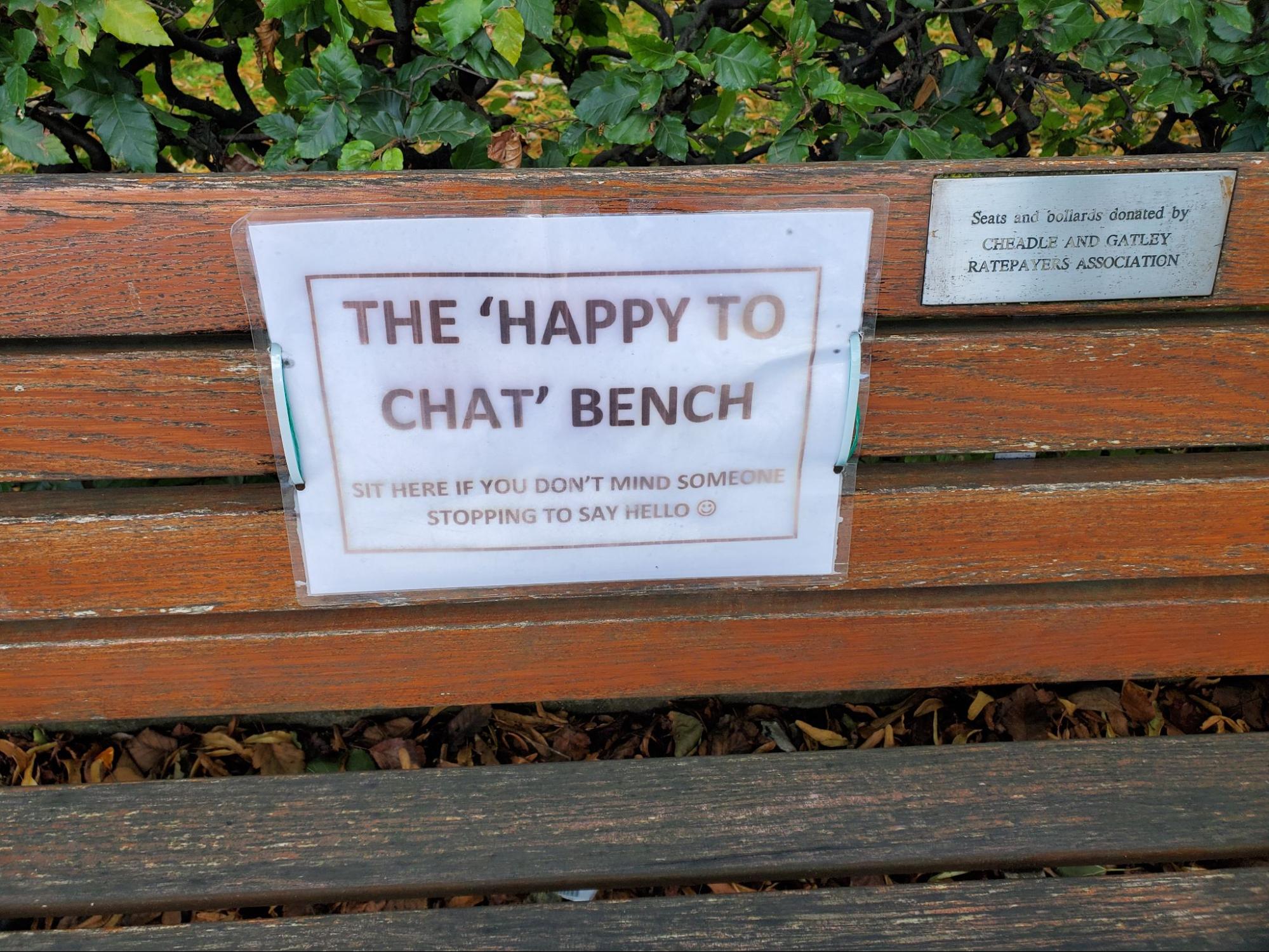 Wooden bench with a sign that says "The 'happy to chat' bench. Sit here if you don't mind someone stopping to say hello"