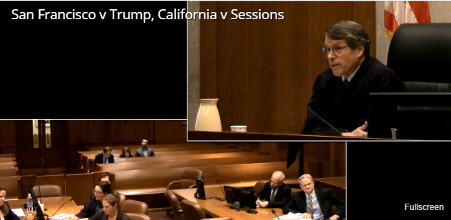 A courtroom scene from San Francisco v. Trump and California v. Sessions at the Phillip Burton Courthouse in San Francisco, CA. Judge Edward Chen presides over the case from the bench. Various angles capture attorneys presenting arguments and members of the public observing. This recording is part of a special camera pilot program allowing cameras in the courtroom.