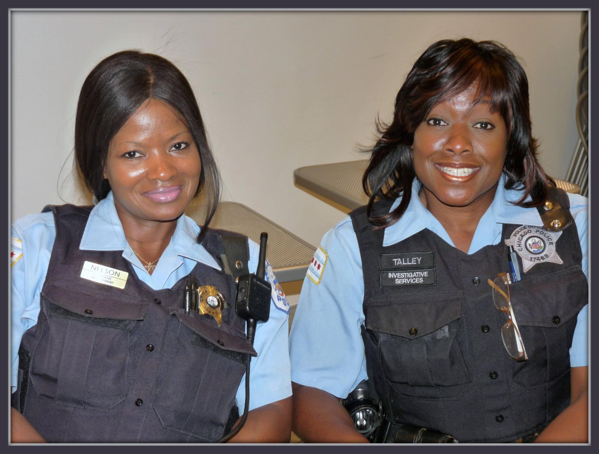Two dark skinned female police officers smiling warmly at the camera.