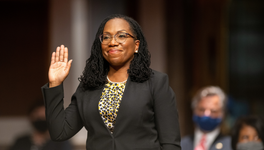 Justice Ketanji Brown Jackson smiling and raising her right hand in a black suit with a printed top underneath as she's sworn in as the 116th Supreme Court justice, marking a significant milestone towards diversity and inclusion.