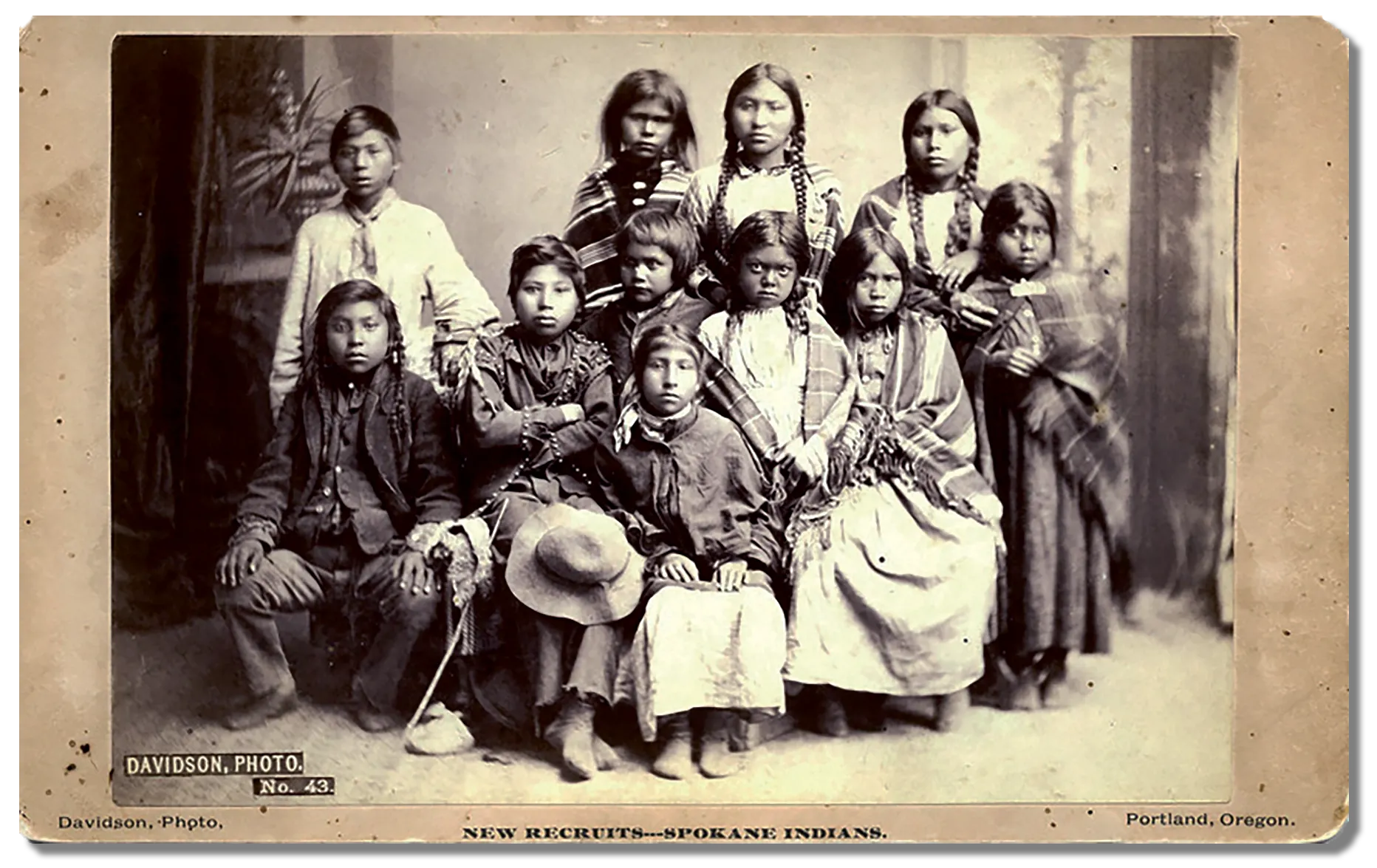 A group portrait of students from the Spokane tribe at the Forest Grove Indian Training School, Eleven young students from the Spokane tribe are gathered together for a photo, fear and distrust is evident in their facial expressions.