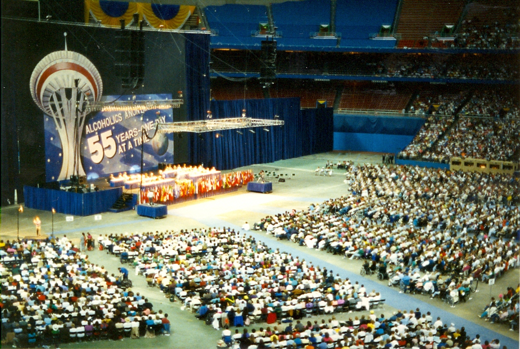 A crowded convention center features a large replica of the Space Needle that says "Alcoholics Anonymous - 55 Years - one day at a time"