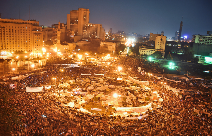 an aerial or high-rise view of an enormous crowd and temporary tents in a city public area. the image is taken at night.