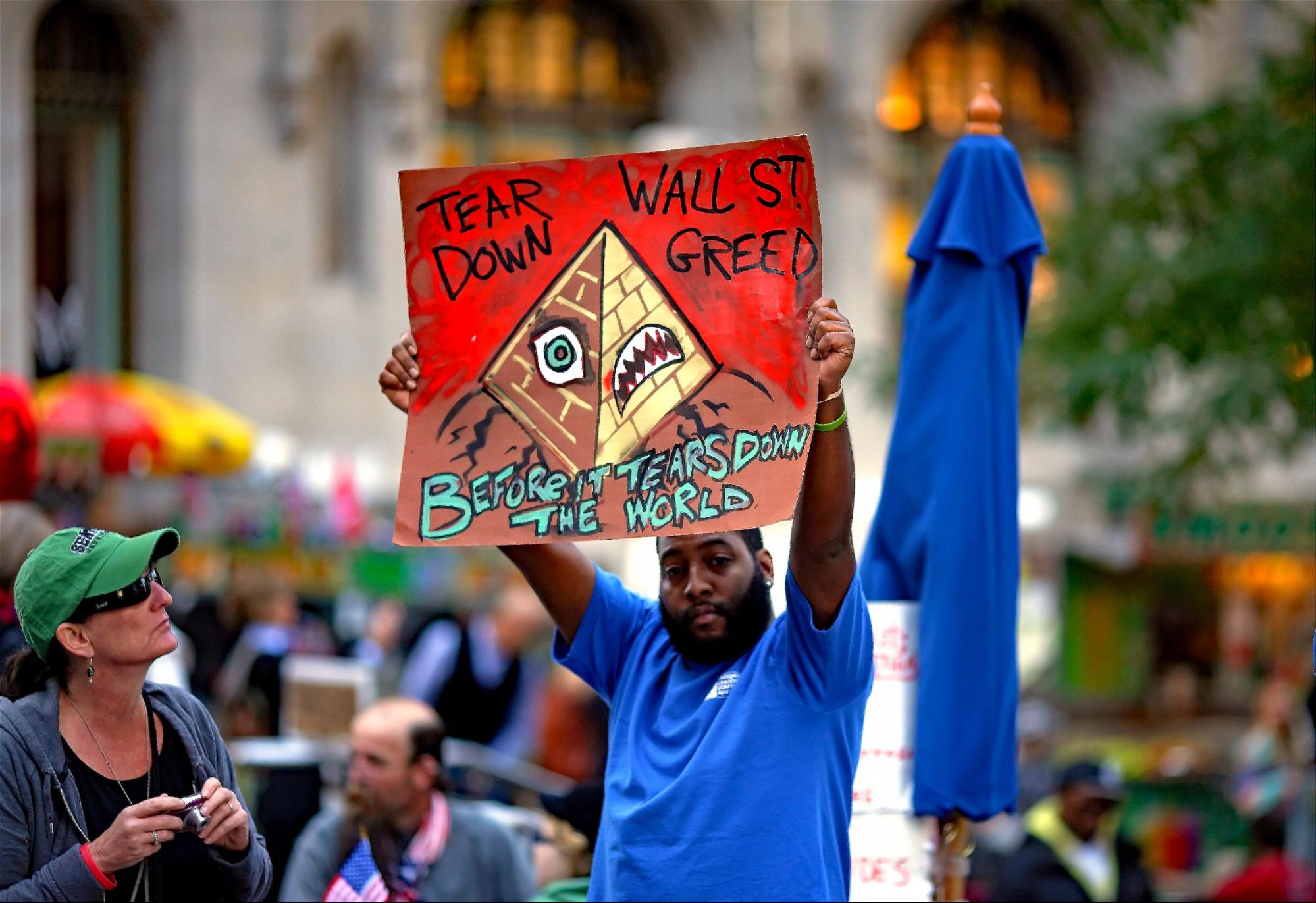 a man with dark skin stands in public holding a sign