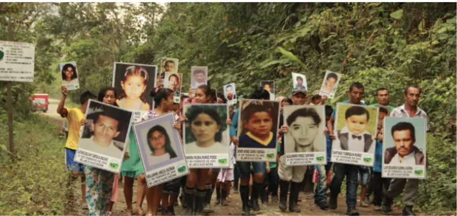 A group of 15-20 people walk together carrying large pictures of the people they have lost to violence.