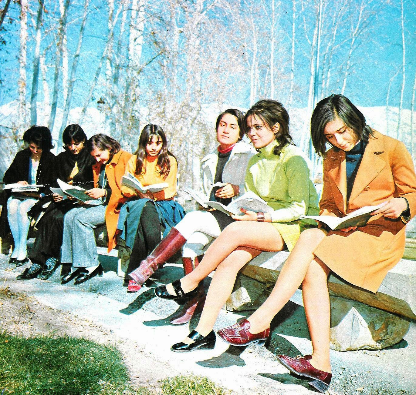 seven women with dark hair in modern fashions from 1970s studying outside.