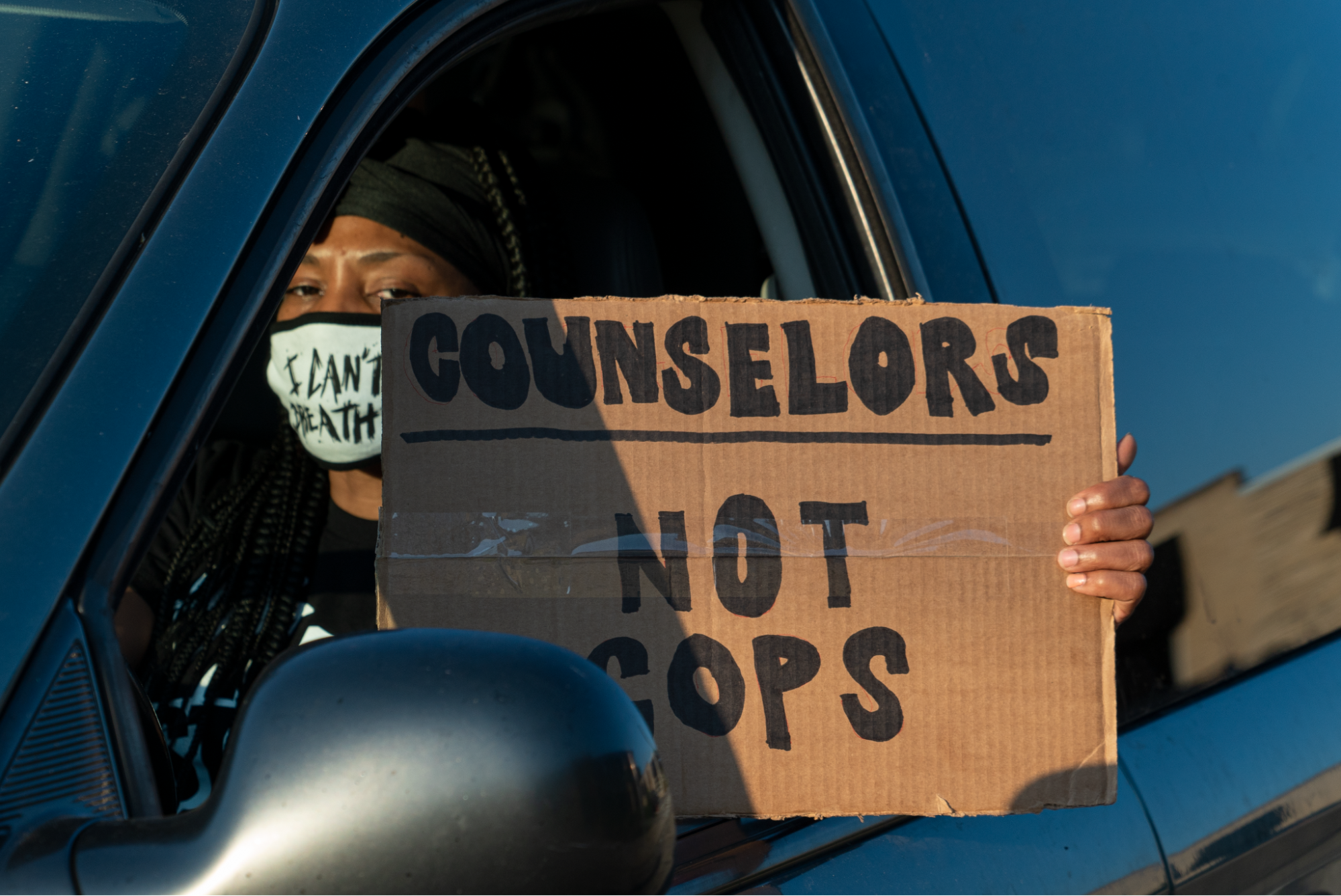 A protester in Milwaukee wears a mask with a slogan "I can't breathe, while holding a sign that says "counselors, not cops".