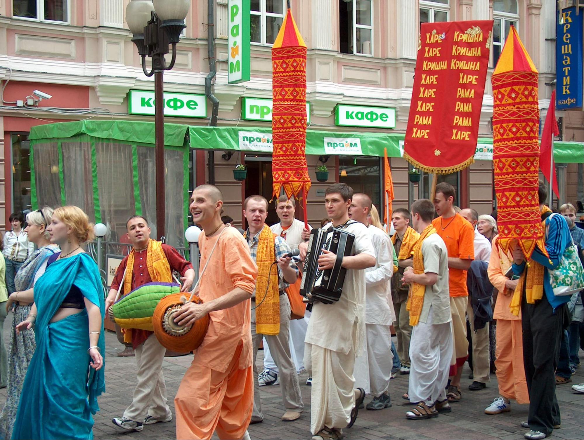 A dozen people with light-skin in robes carry banners and play drums and accordions in the street