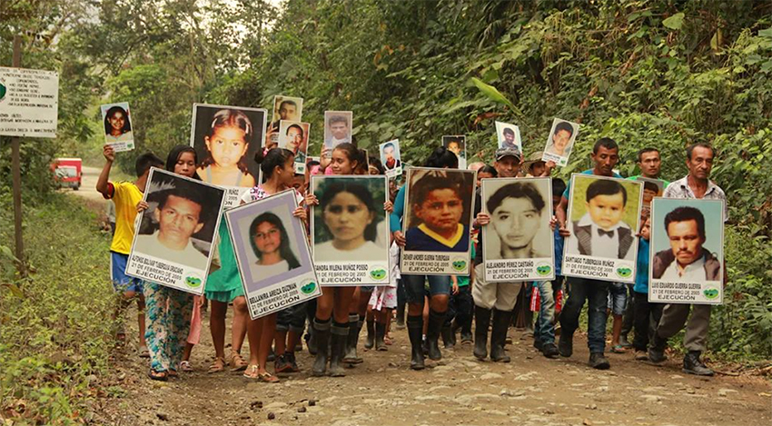 A group of 15-20 people walk together carrying large pictures of the people they have lost to violence.