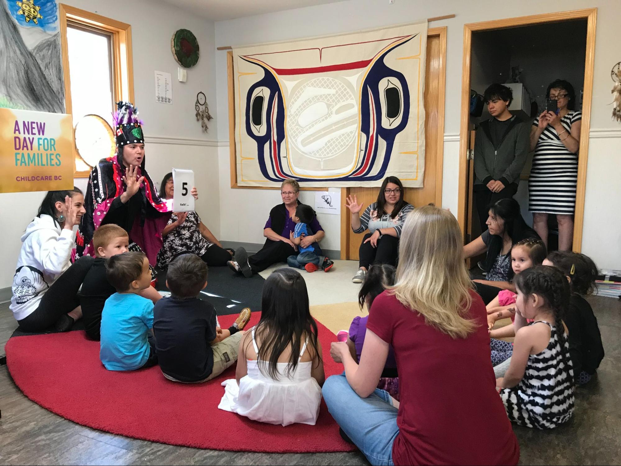 A group of children and adults sit in a circle and engage in indigenous centered learning.