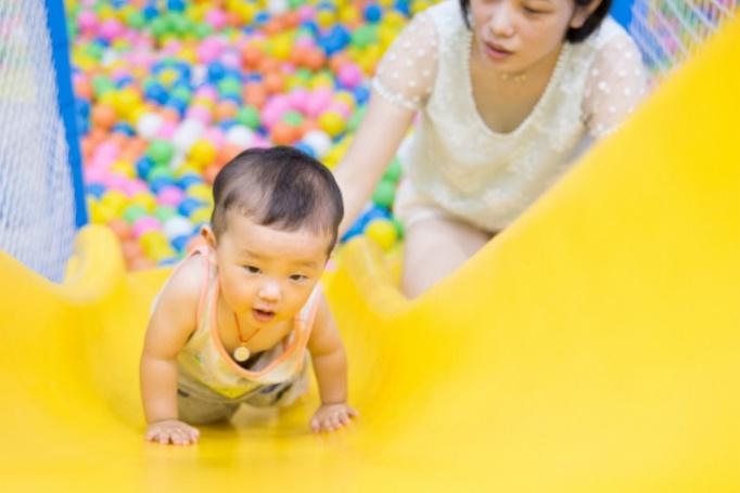 Asian toddler plays with mother on a slide leading to a ball pit