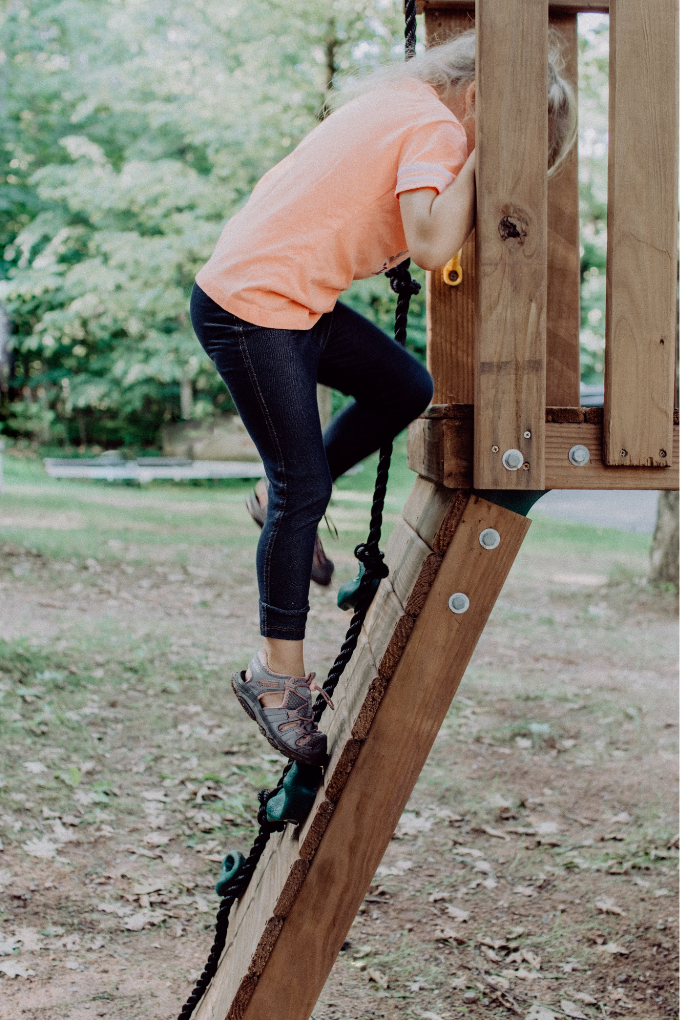 A White child climbs on a wooden structure presumably in a playground