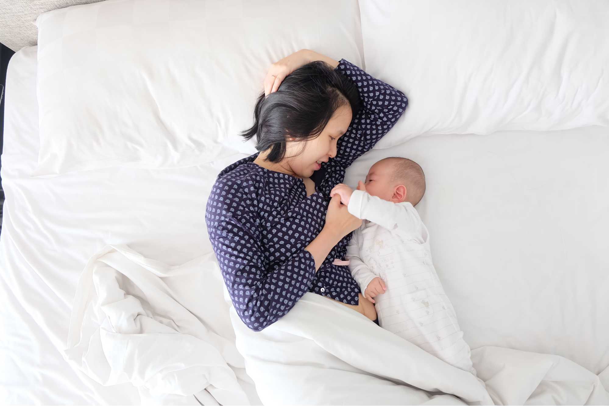 An Asian mother lays in bed next to her newborn baby.