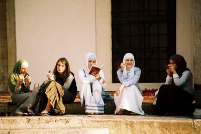 A group of young adults sits on a step and socializes while reading and drinking tea.