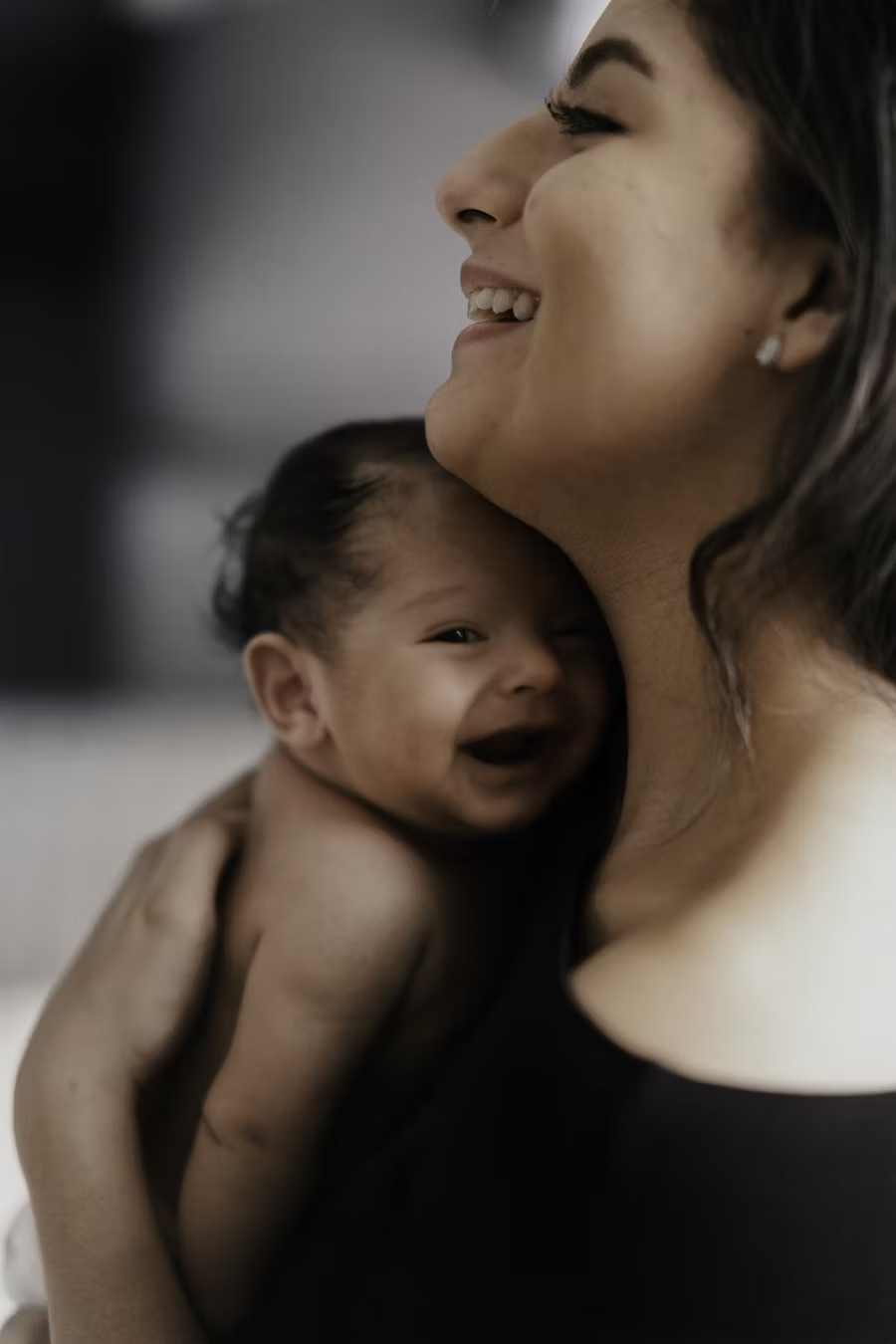 A woman of Hispanic heritage smiles and holds a smiling baby