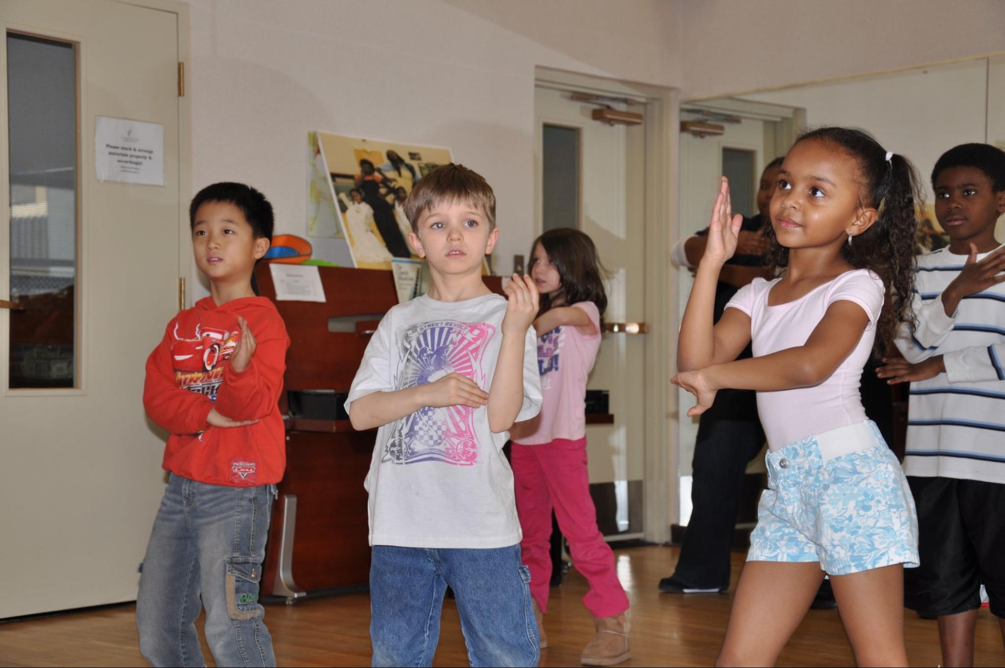 Children of various ethnicities, Asian, White, and Black, learn line dancing