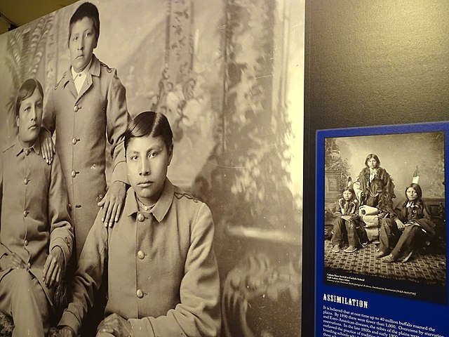 Three Indigenous boys wearing European clothing are depicted aside a picture of them in their Indigenous clothing