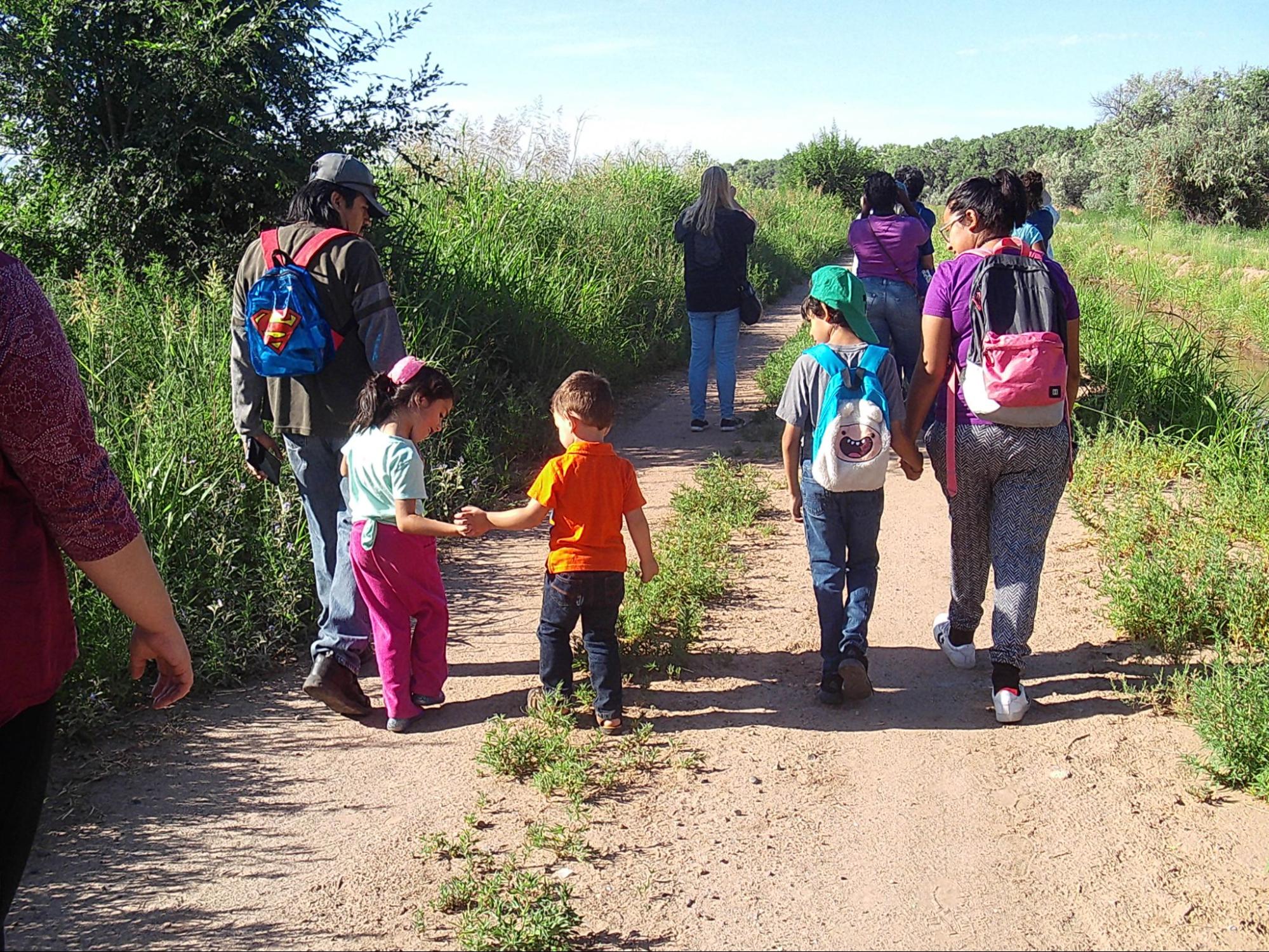 A family that appears Hispanic walks with three children and other adults on a path through a grassy park