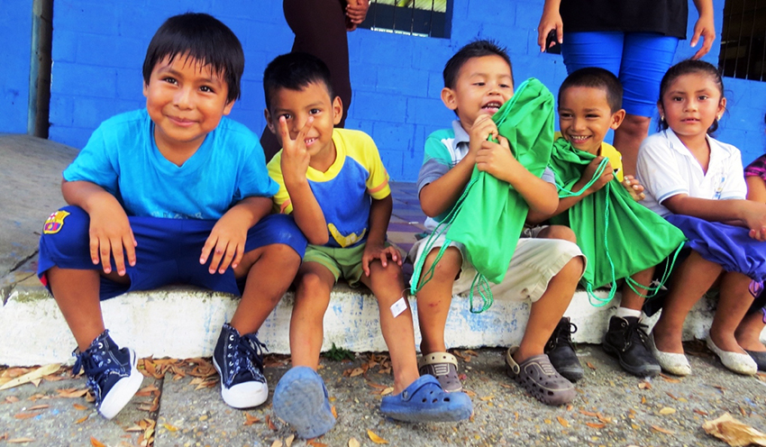 Five children of color sit next to each other on a curb, smiling