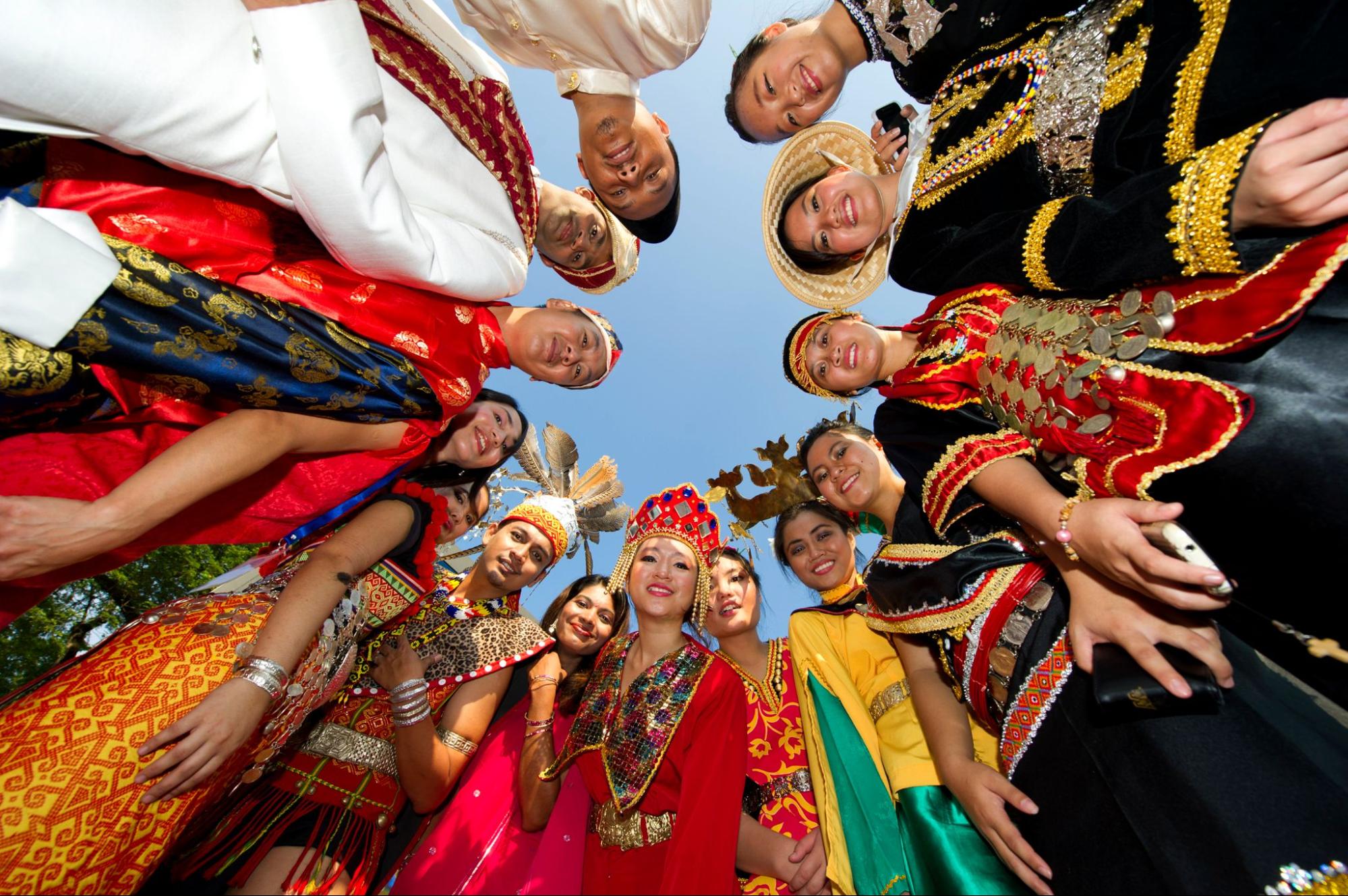 A group of individuals wearing various cultural clothing pieces are in a circle looking down at the camera.